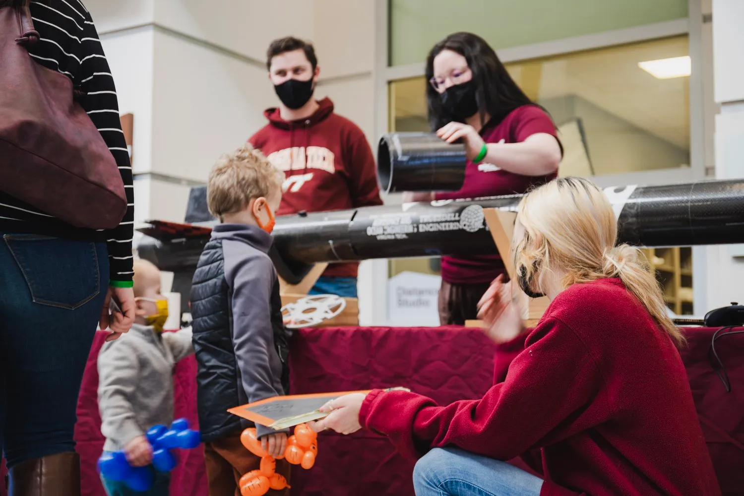 A group of children and Rocketry at Virginia Tech members looking and touching parts of the rocket at a booth